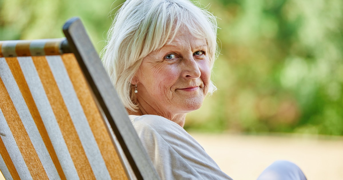 Glückliche Rentnerin auf Strandstuhl die ihr Haus verrentet hat